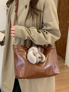 Brown vintage large shoulder bag with plush bunny charm shown on model in a minimalist room