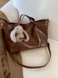 Large dark brown vintage tote bag in glossy leather on sofa with plush rabbit charm