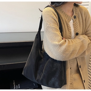 Close-up of a large black leather hobo tote bag worn with a beige knitted sweater