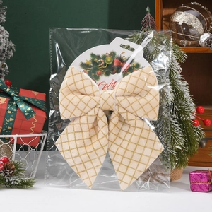 Detail of a beige gold-grid Christmas bow ornament in its holiday themed packaging