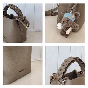 Détail du sac seau taupe montrant l'anse tressée, le logo métal et le charm ours