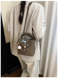 Détail du sac seau en cuir gris avec poignée tressée et charmant pendentif d'ours brun