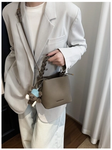 Détail du sac seau en cuir marron foncé avec logo doré, chaîne et breloque ours