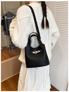 Detail of black pebbled leather bucket bag with top handle and metal lock closure