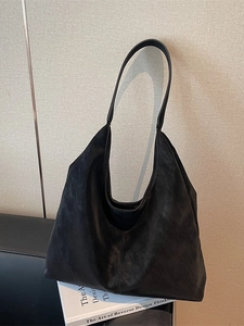 Minimalist large black leather tote bag with curved top and central seam on books