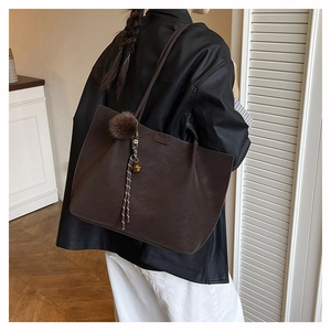 Detail of a large dark brown tote bag with a plush charm accessory on a model