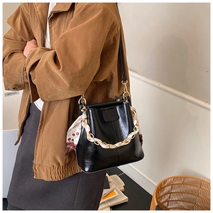 Detail of black bucket bag with gold chain and cherry print silk scarf accent