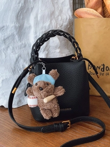 Sac seau noir chic avec poignée tissée et breloque ours en peluche sur table en bois