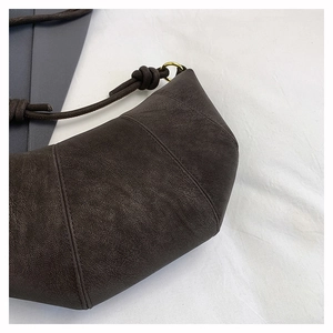 Detailed macro view of dark brown faux suede croissant bag with knotted strap and brass rings