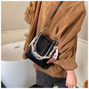 Detail of black glossy bucket bag featuring silk scarf handle and gold chain hardware