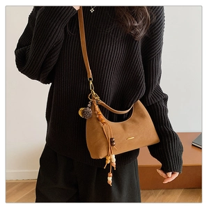 Detail of brown crescent shoulder bag with matte texture and ethnic beaded tassel charm