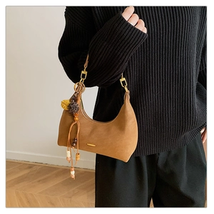 Detail einer braunen Hobo-Tasche aus Leder mit Boho-Anhänger und goldener Hardware