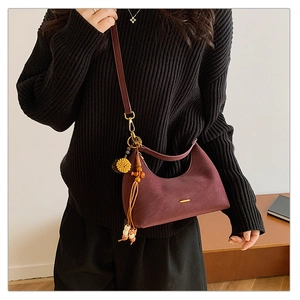 Detail of burgundy crescent hobo bag with gold bar accent and textured tassel charm