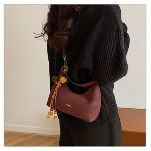 Detail of wine red crescent bag with ethnic pendant and gold metallic trim on shoulder
