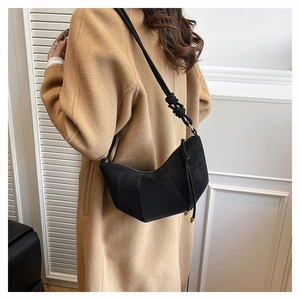 Detail of minimalist black suede crossbody bag with knot strap on a wool coat