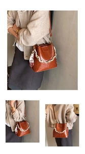 Detail of brown vintage bucket bag with metal chain, printed scarf and long shoulder strap