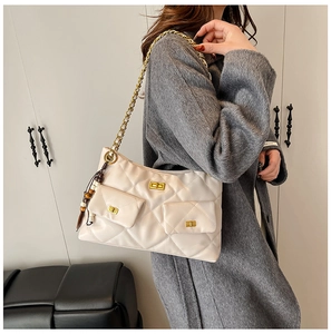Detail of beige quilted shoulder bag with gold chain strap and bead charm on a model