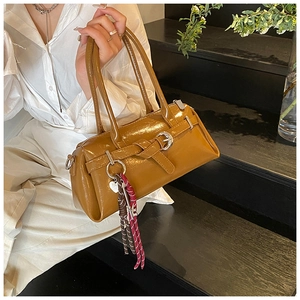 Close-up of caramel brown patent leather handbag with decorative belt and braided charm
