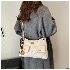 Detail of cream quilted shoulder bag with chain strap and ethnic tassel on grey coat