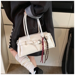 Detail of white baguette bag with decorative belt strap and woven key charm pendant