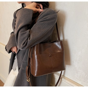 Detail of a brown leather bucket bag with adjustable strap on a grey wool coat