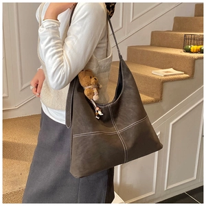 Detail view of large dark brown tote bag with white contrast stitching and bear charm
