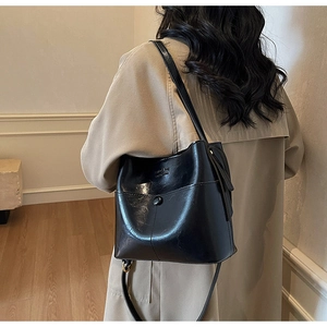 Detail of a black leather bucket bag with drawstring closure and vertical stitching decor