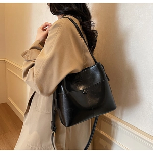 Detail view of black glossy leather bucket bag with metallic snap and thin shoulder strap
