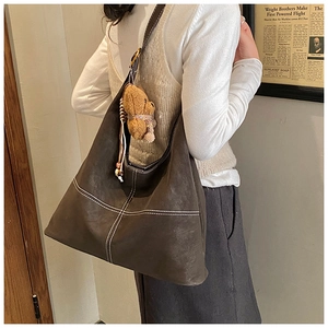 Detail of deep brown tote bag featuring contrast stitching and a plush bear charm