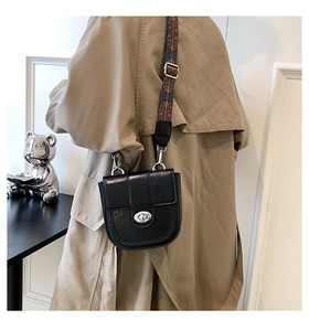 Detail of black glossy saddle bag featuring a silver oval buckle and ethnic embroidered strap
