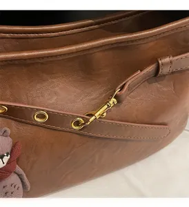 Détail du sac bandoulière en cuir marron avec fermoir doré et charme d'ours