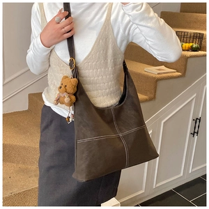 Detail of dark brown leather tote with white stitching and bear plush charm