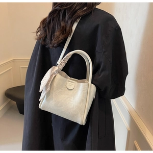 Detail of cream bucket bag showing woven handle and geometric silk scarf decoration