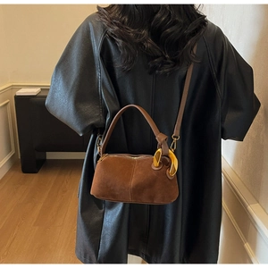 Detail of a brown suede Boston bag with artistic large gold metal ring handles and strap
