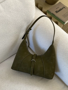 Minimalist olive green suede shoulder bag with adjustable strap on a white sofa