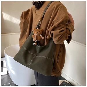 Detail of dark green large tote bag with white stitching and plush bear charm