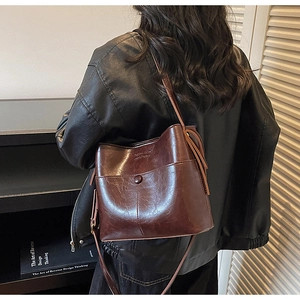 Detail of a large brown leather bucket bag with a stylish tassel charm and front pocket