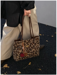 Detail of leopard print plush tote bag with woven handles and furry ball charm in autumn street