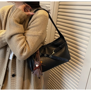Sac sous le bras en cuir noir avec un porte-clé ours en peluche marron porté par un mannequin