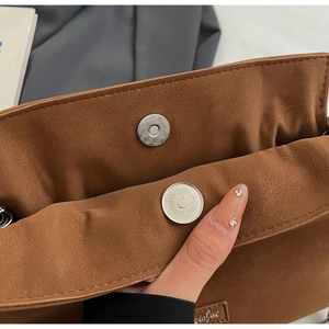 Detailed macro view of the magnetic closure on the brown matte leather bucket bag