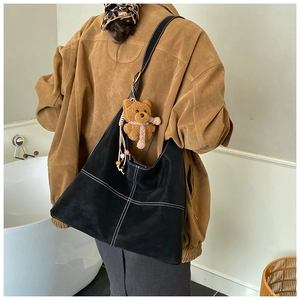Detail of black leather tote bag with white contrast stitching and plush bear charm