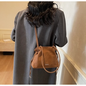 Close-up of brown leather drawstring bucket bag featuring a metallic logo and pleated design