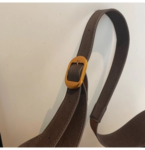Close-up of brown textured leather shoulder strap with golden oval buckle for bucket bag