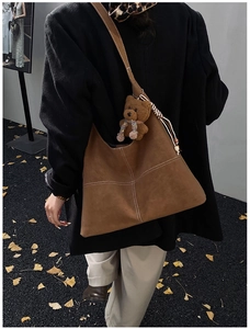 Brown suede tote bag with white contrast stitching and bear charm in autumn street scene