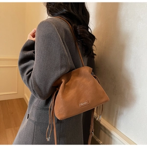 Detail of a brown matte suede bucket bag with drawstring and metal logo on a model