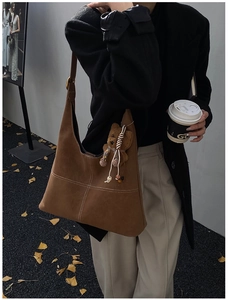 Brown suede tote bag detail with white cross-stitching and a cute plush bear charm