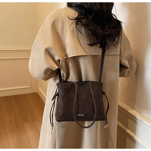 Close-up of dark brown frosted leather bucket bag with brand plaque on female model
