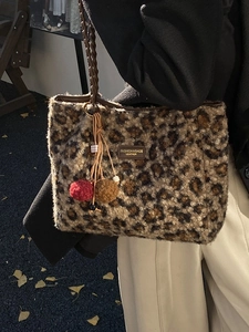 Leopard print plush tote bag with woven handles and furry charm shown in autumn street scene