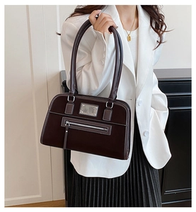 Détail du sac à bandoulière marron foncé avec surpiqûres blanches et plaque argentée