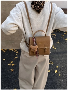 Detail of a brown leather mini backpack with metal buckle and plush bear pendant in street style